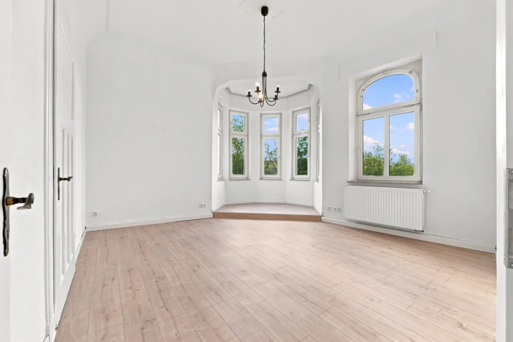 Heller Wohnraum mit Holzboden, hohen Fenstern und polygonalem Erker