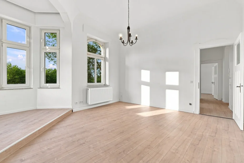 Wohnraum mit Holzboden, hohen Fenstern und angrenzendem Erkerbereich