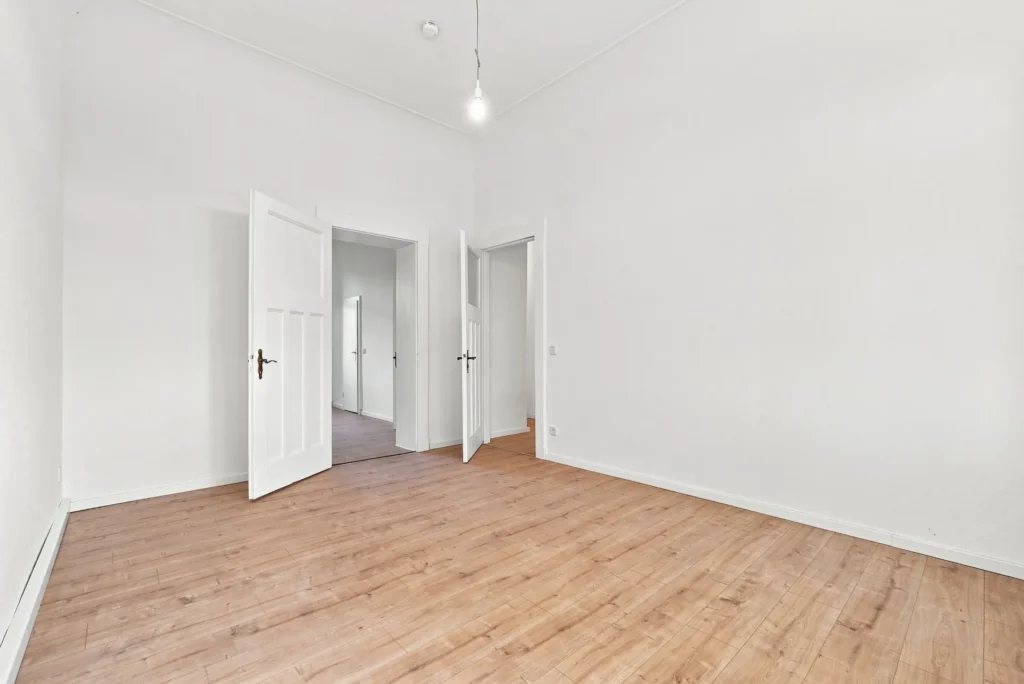 Leerer Altbau-Raum mit Holzboden, hohen Decken und weißen Kassettentüren