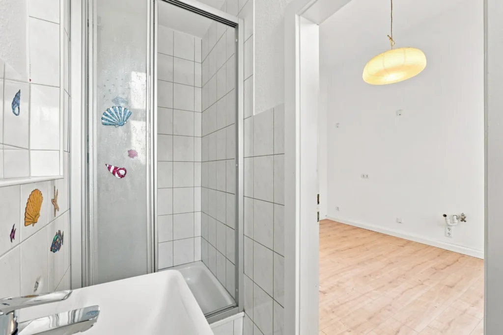 Kleines Badezimmer mit Waschbecken, Dusche und angrenzendem Küchenraum