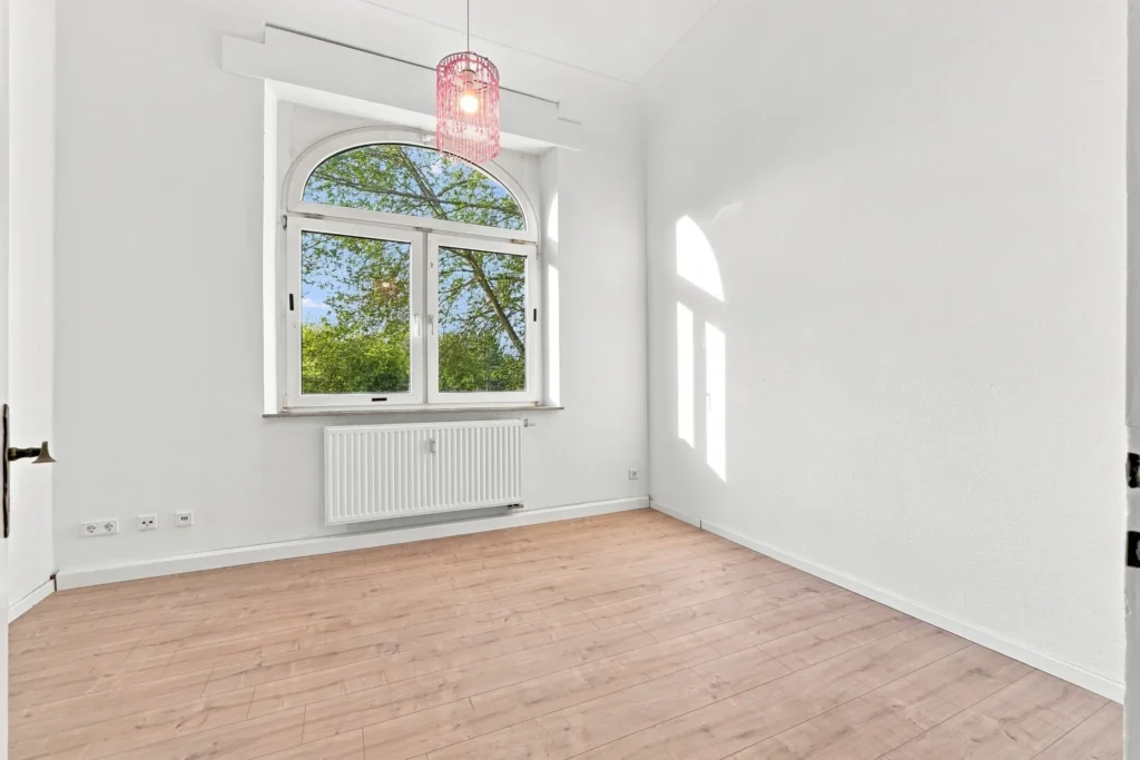 Heller Raum mit Holzboden und großem Rundbogenfenster mit Blick ins Grüne