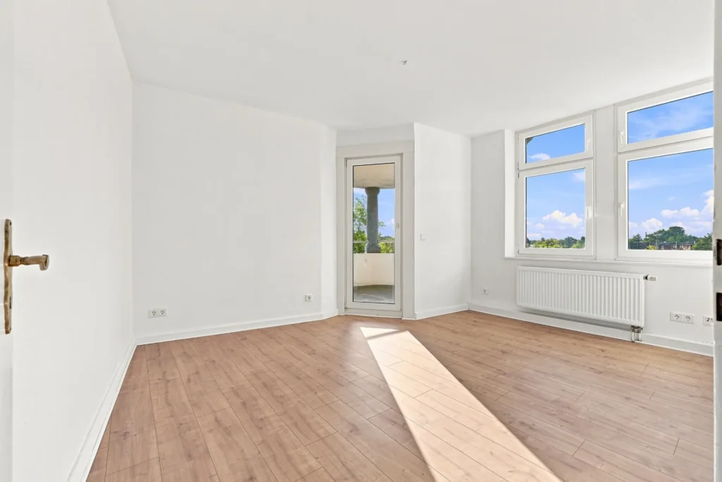 Heller Wohnraum mit Holzboden, großer Fensterfront und Zugang zum Balkon