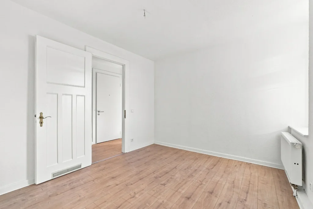 Leerer Raum mit Holzboden, weißen Türen und Heizkörper am Fenster